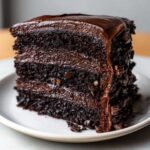 A decadent slice of moist chocolate fudge cake layered with rich chocolate frosting and covered in chocolate chips.
