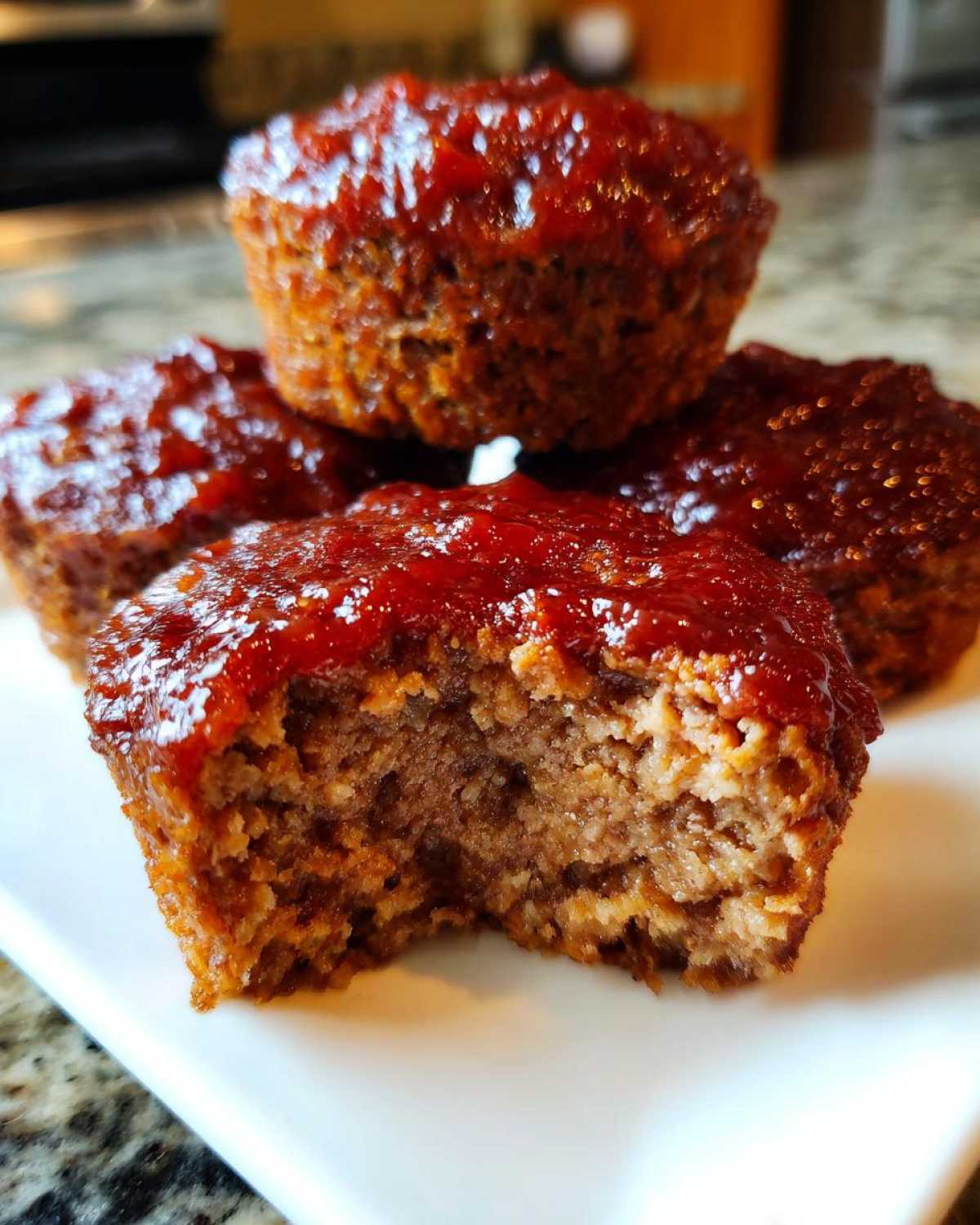 Close-up of several glazed mini meatloaf portions, one with a bite taken out to reveal the moist interior.