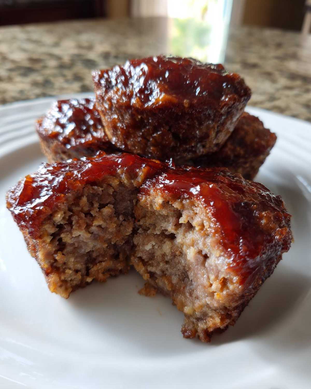 Close-up of a moist mini meatloaf cut open, showing the texture and shiny glaze topping.