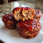 Close-up of several moist mini meatloaf portions stacked, showing the texture and shiny glaze topping.