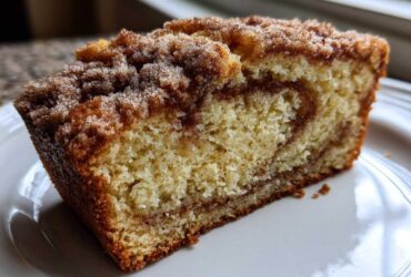 Close-up of a moist slice of snickerdoodle zucchini bread with a cinnamon swirl and crumb topping.