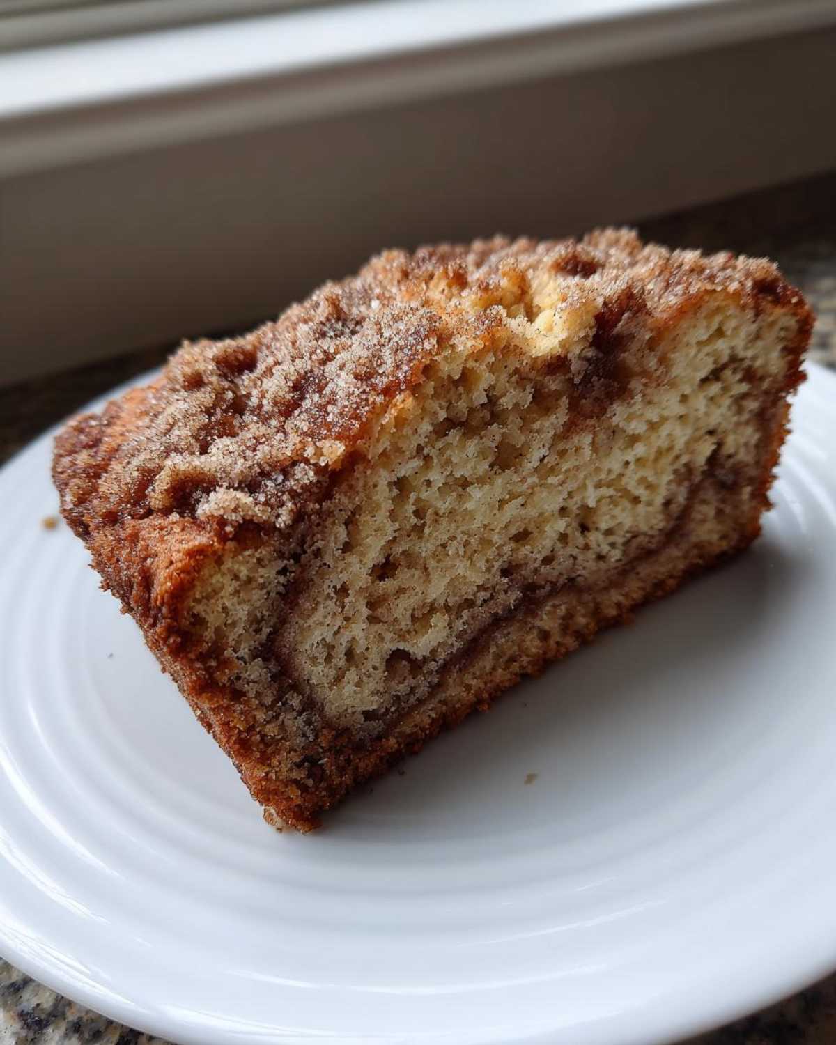 A moist slice of snickerdoodle zucchini bread with a cinnamon swirl and sugary topping on a white plate.