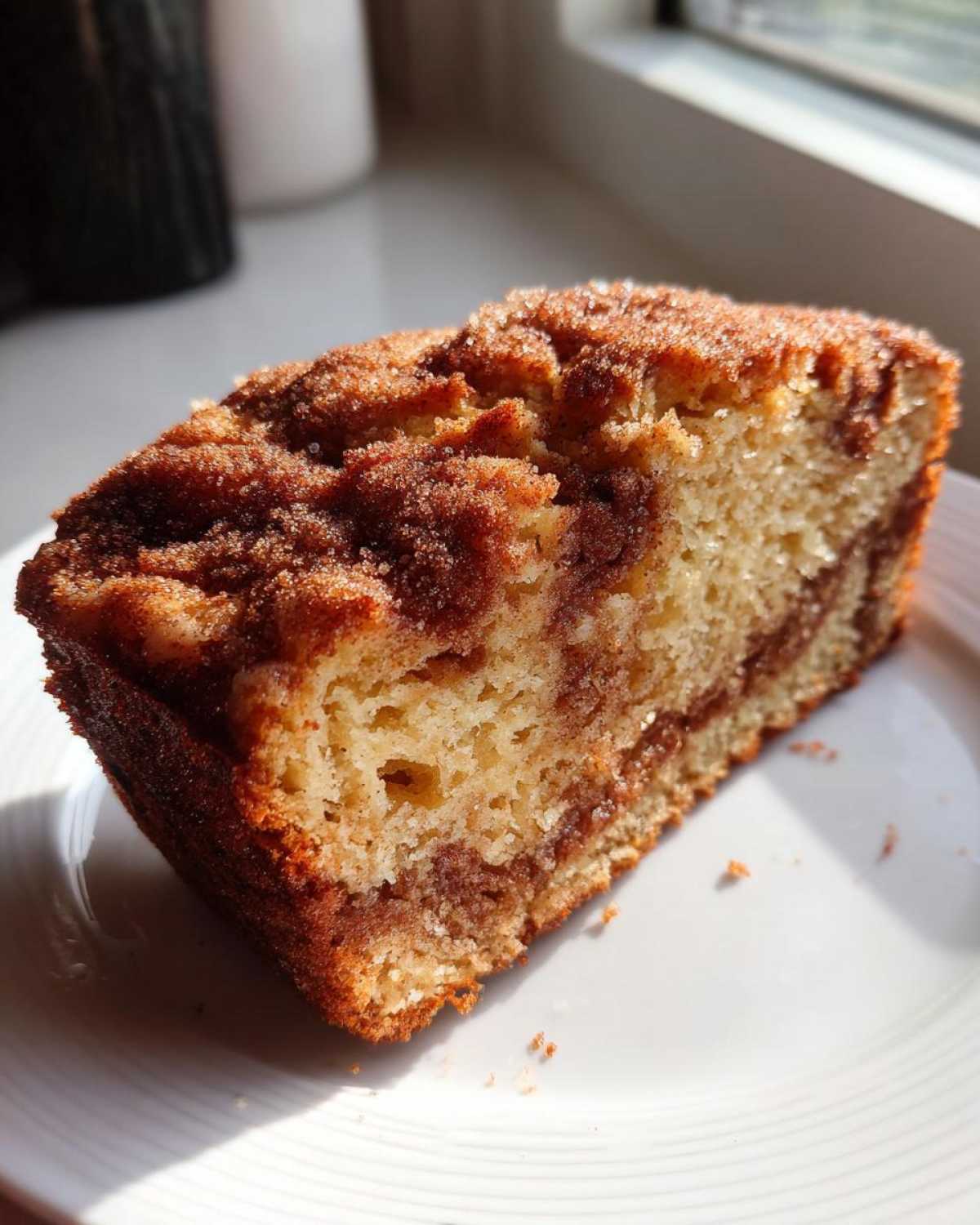 A close-up slice of moist snickerdoodle zucchini bread featuring a cinnamon swirl and sugary topping, sitting on a white plate.