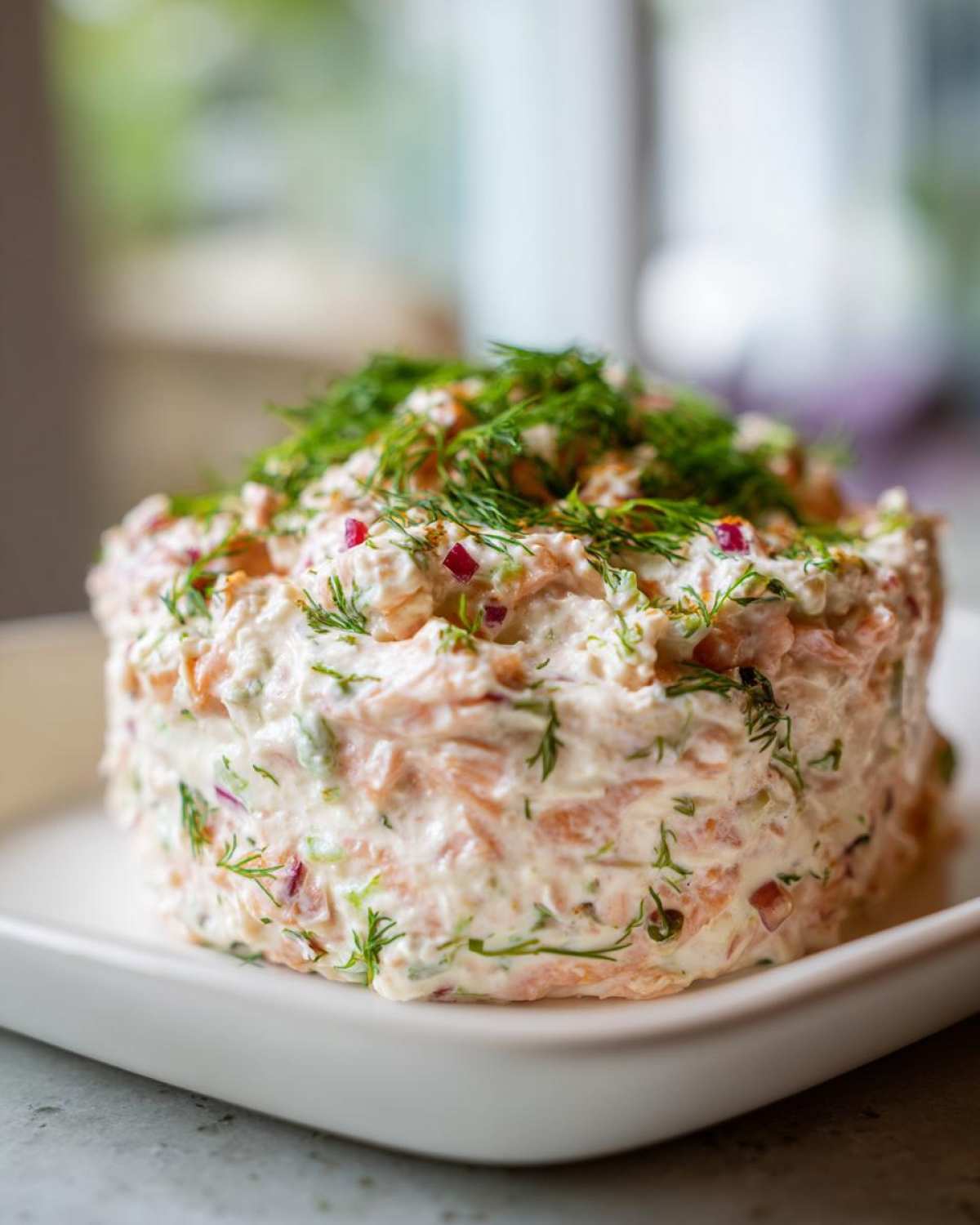 A molded serving of creamy smoked salmon dip mixed with red onion and topped generously with fresh dill.