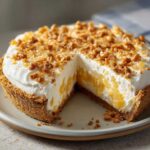 A creamy, no-bake million dollar pie with a graham cracker crust, showing a slice removed to reveal the filling and topping.