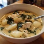 Close-up of a white bowl filled with creamy olive garden chicken gnocchi soup, featuring large gnocchi and spinach.