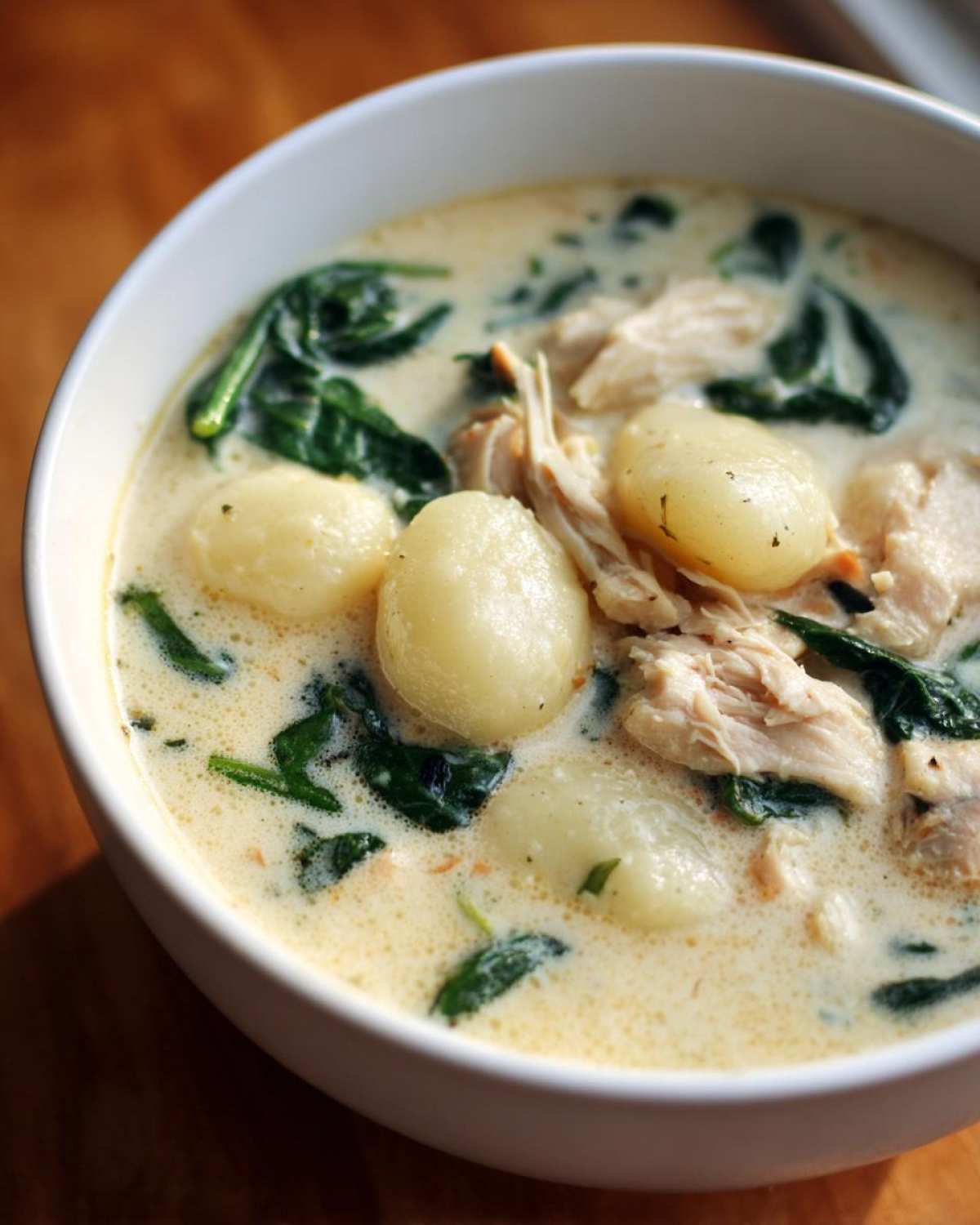 Close-up of a white bowl filled with creamy olive garden chicken gnocchi soup, showing gnocchi, shredded chicken, and spinach.