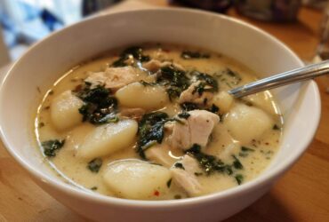Close-up of a white bowl filled with creamy olive garden chicken gnocchi soup, featuring large gnocchi and spinach.