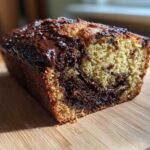 A close-up of a freshly baked chocolate bread loaf with a marbled interior and melted chocolate glaze on top.