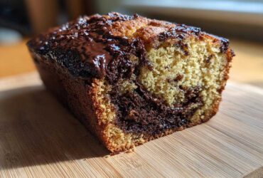 A close-up of a freshly baked chocolate bread loaf with a marbled interior and melted chocolate glaze on top.