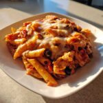 A close-up serving of creamy enchilada pasta topped with melted white cheese on a square white plate.