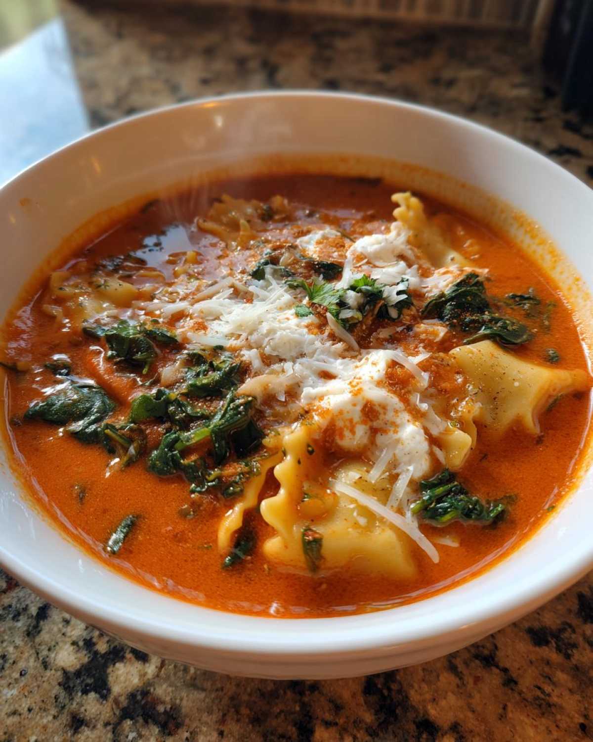 A close-up of a steaming white bowl filled with rich, creamy one pot lasagna soup, topped with ricotta and shredded cheese.