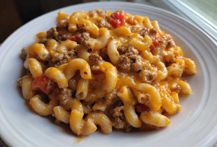 Close-up of a serving of cheesy taco pasta with elbow macaroni, ground beef, and tomatoes on a white plate.