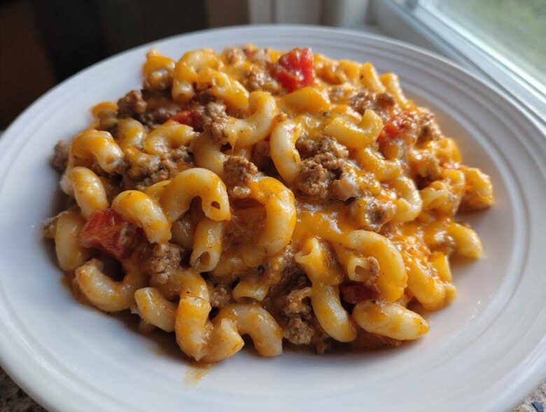 Close-up of a serving of cheesy taco pasta with elbow macaroni, ground beef, and tomatoes on a white plate.