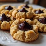 A plate of freshly baked peanut butter blossom cookies with a dollop of melted chocolate in the center.