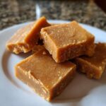 Close-up of several squares of rich, brown penuche fudge piled on a white plate.