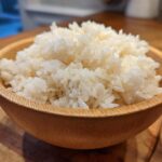 Close-up of perfectly seasoned sushi rice piled high in a small, light brown wooden bowl.