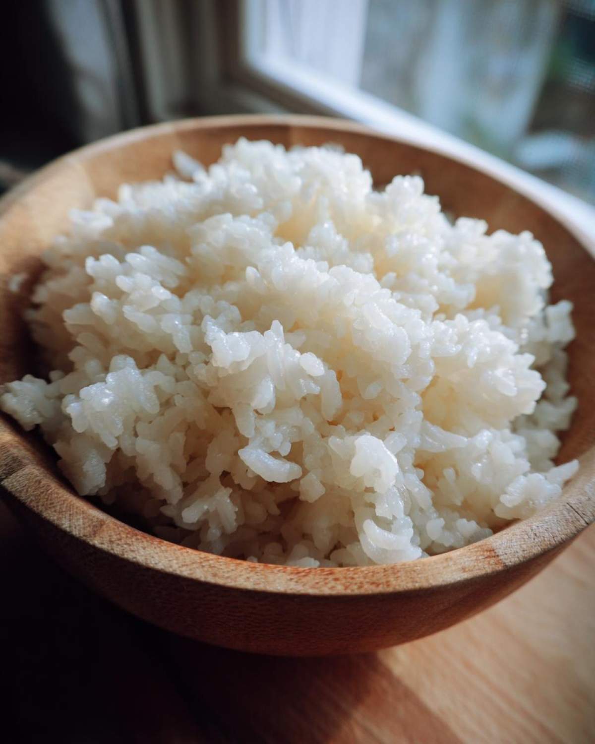Close-up of perfectly cooked, glossy sushi rice piled high in a small wooden bowl.