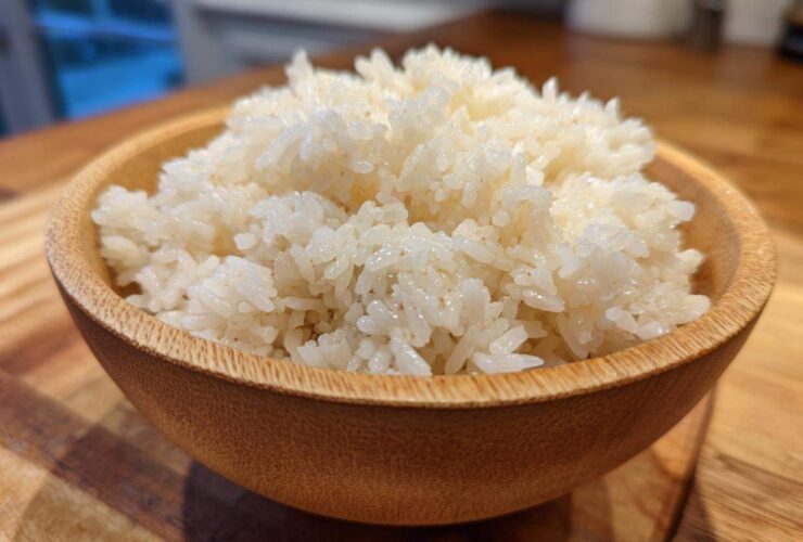 Close-up of perfectly seasoned sushi rice piled high in a small, light brown wooden bowl.
