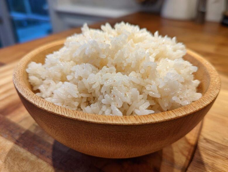 Close-up of perfectly seasoned sushi rice piled high in a small, light brown wooden bowl.
