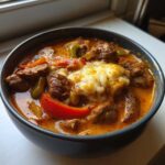 A close-up of a hearty bowl of philly cheese steak soup featuring beef chunks, peppers, and a dollop of melted cheese.