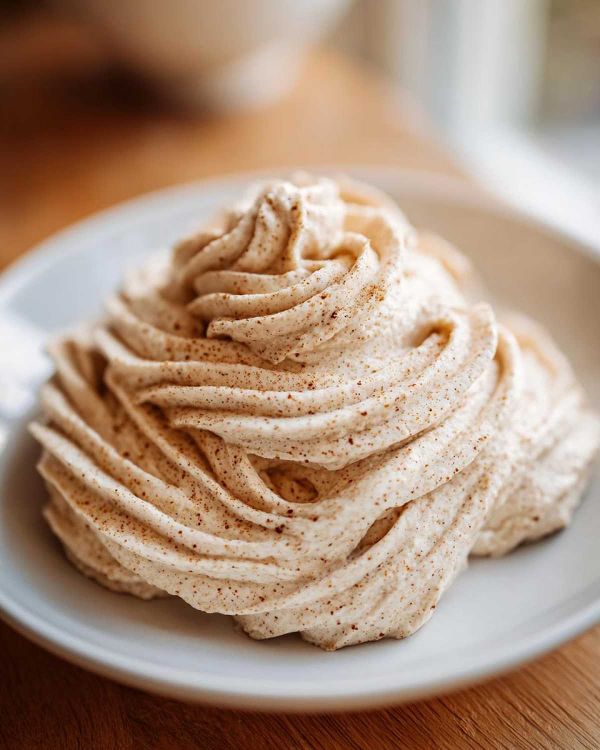 Close-up of perfectly piped cinnamon butter, speckled with ground cinnamon, on a small white plate.