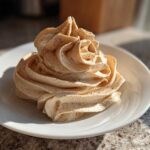 A beautiful swirl of light brown cinnamon butter, dusted with extra cinnamon, served on a small white plate.