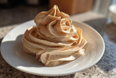 A beautiful swirl of light brown cinnamon butter, dusted with extra cinnamon, served on a small white plate.