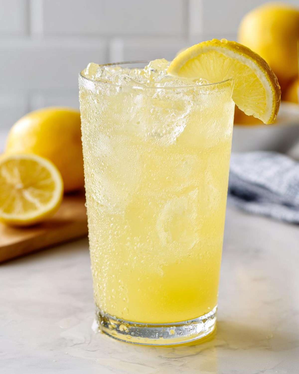 Close-up of a tall, sweating glass filled with cold lemonade, ice, and garnished with a lemon slice.