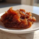 A close-up of thick, glistening, dark amber pear butter served on a small white saucer.