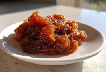 A close-up of thick, glistening, dark amber pear butter served on a small white saucer.