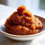 A close-up of a mound of rich, dark brown pear butter, glistening with spices, served in a small white bowl.