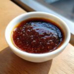 Close-up of thick, glossy homemade teriyaki sauce with visible spice flecks in a small white dipping bowl.