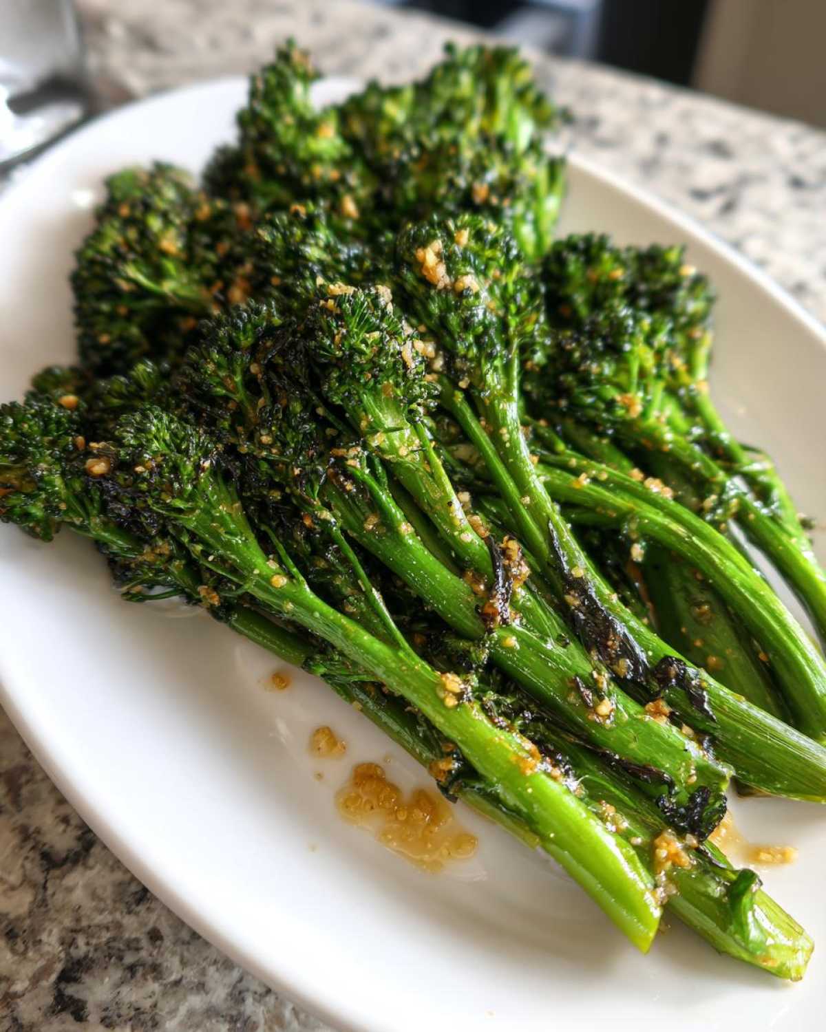 A white platter holding several stalks of bright green, roasted broccolini seasoned with a visible garlic and oil glaze.