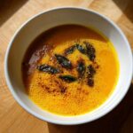 Close-up of bright orange roasted butternut squash soup topped with fried sage leaves and spices.