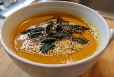 A close-up of creamy roasted butternut squash soup topped with browned butter and crispy sage leaves.