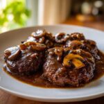 Three juicy Salisbury steak patties covered in rich brown mushroom gravy on a white plate.