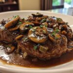 Close-up of two rich Salisbury steak patties smothered in brown mushroom gravy and fresh thyme.