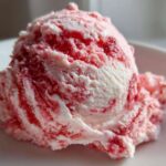 Close-up of a single scoop of homemade strawberry ice cream with visible red swirls on a white plate.