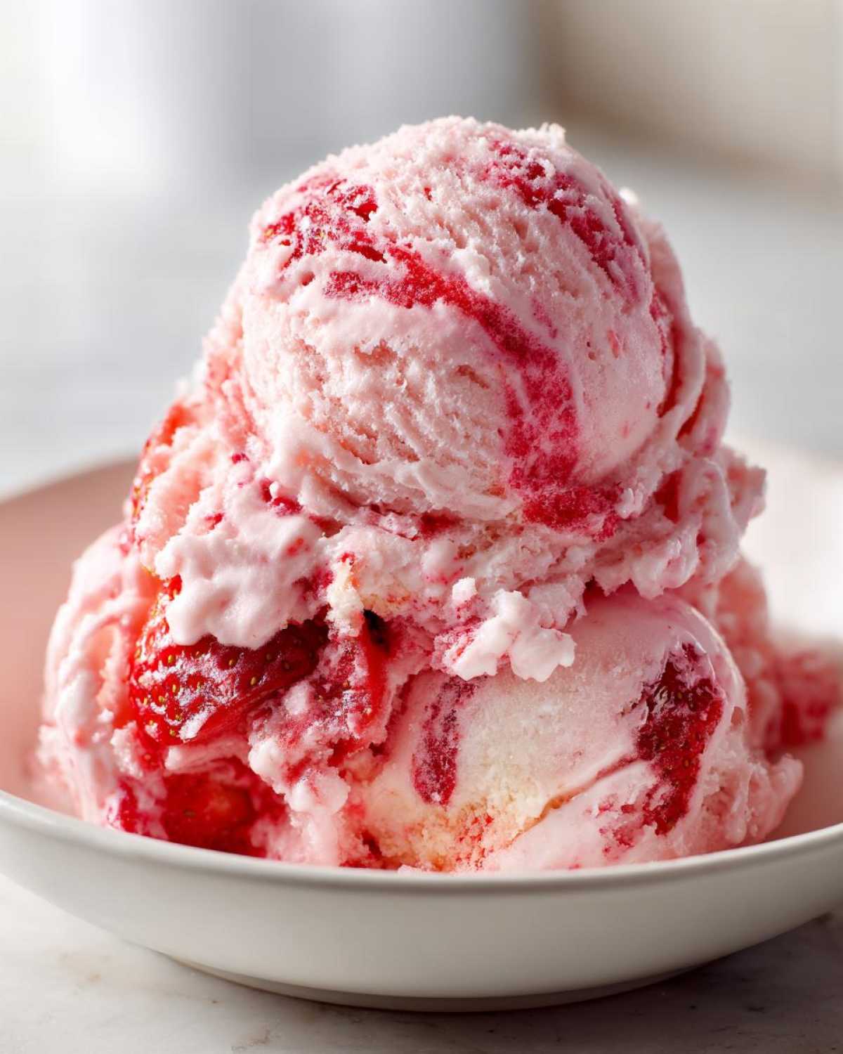 Close-up of several scoops of pink and white strawberry ice cream with visible strawberry swirls in a white bowl.