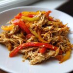 Close-up of shredded chicken mixed with colorful strips of red, yellow, and green bell peppers, ready for crockpot chicken fajitas.