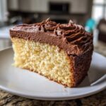 A close-up of a slice of yellow cake topped with thick, piped chocolate frosting.
