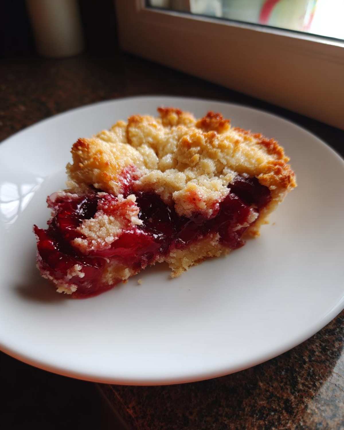 A close-up of a serving of cherry dump cake with a crumbly topping on a white plate.