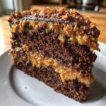 Close-up of a moist slice of german chocolate cake recipe showing dark chocolate layers and thick coconut-pecan frosting.