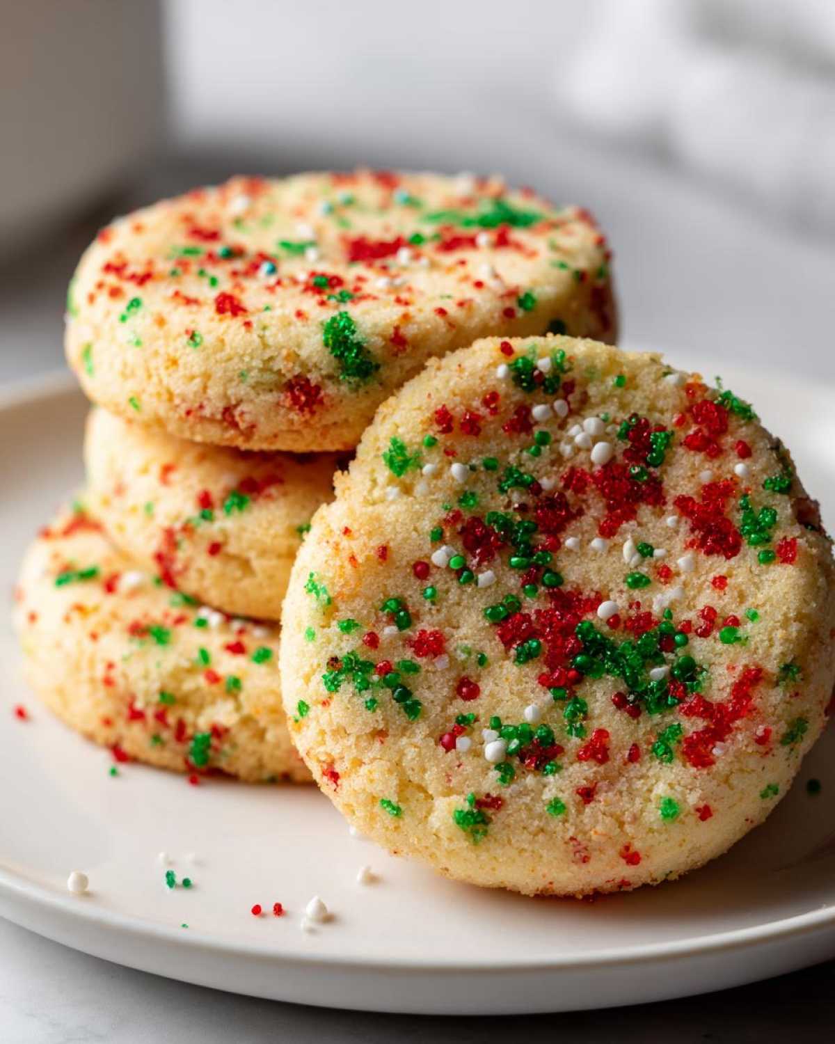 A stack of soft christmas sprinkle sugar cookies topped with red, green, and white holiday sprinkles.