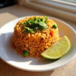 A perfectly molded serving of vibrant orange Spanish rice, topped with cilantro and served with a lime wedge.