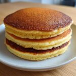 A stack of three golden brown almond flour pancakes served on a light gray plate.