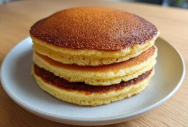 A stack of three golden brown almond flour pancakes served on a light gray plate.