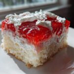 Close-up of a moist slice of strawberry jello poke cake layered with cream and topped with whipped cream.