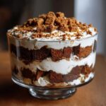 A stunning, layered gingerbread trifle featuring dark cake cubes and thick white cream, topped with crumbled gingerbread pieces.